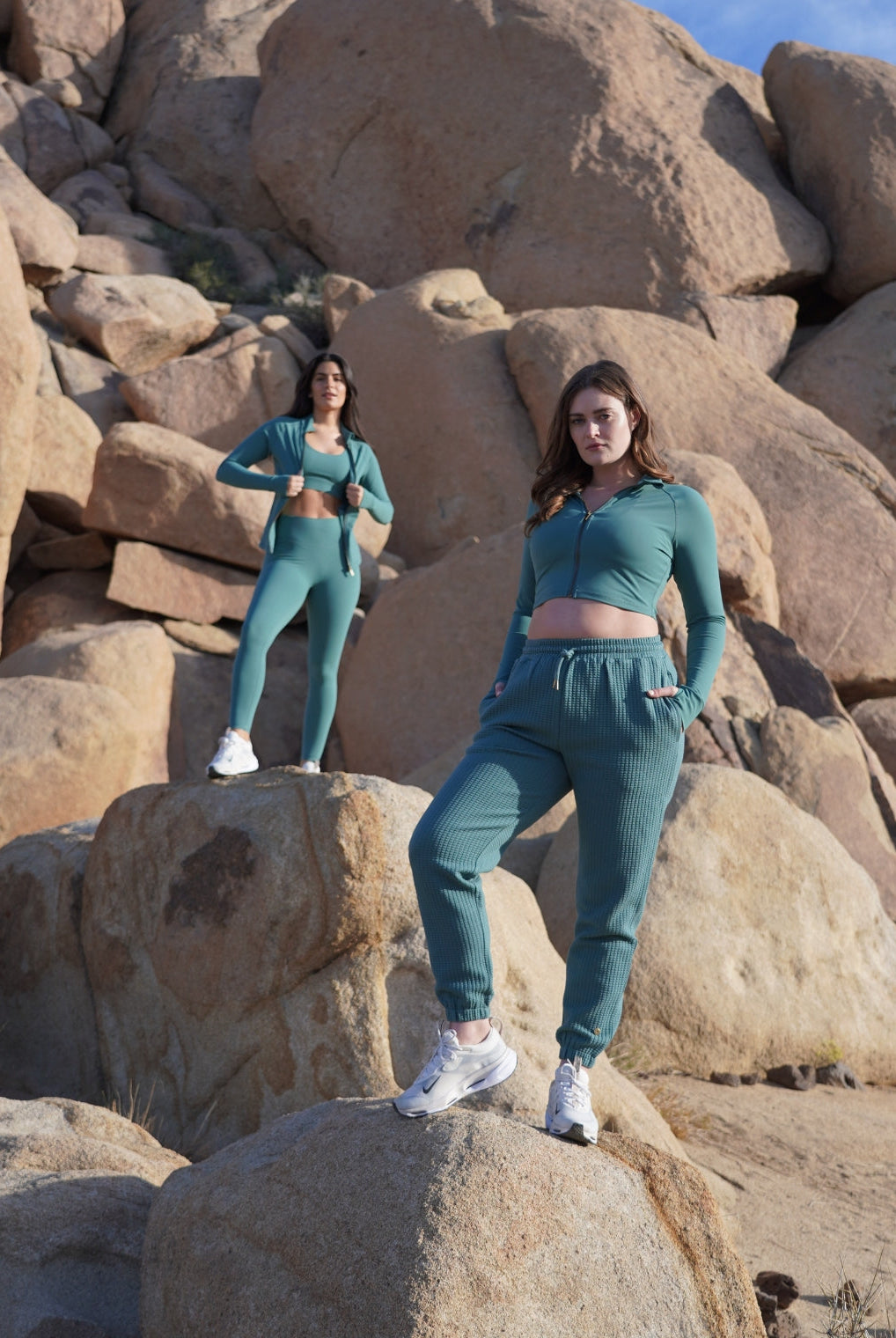 Photograph features 2 models standing on big rocks wearing Love Fitness Sedona Collection outfits of pieces in the Mineral color-way.