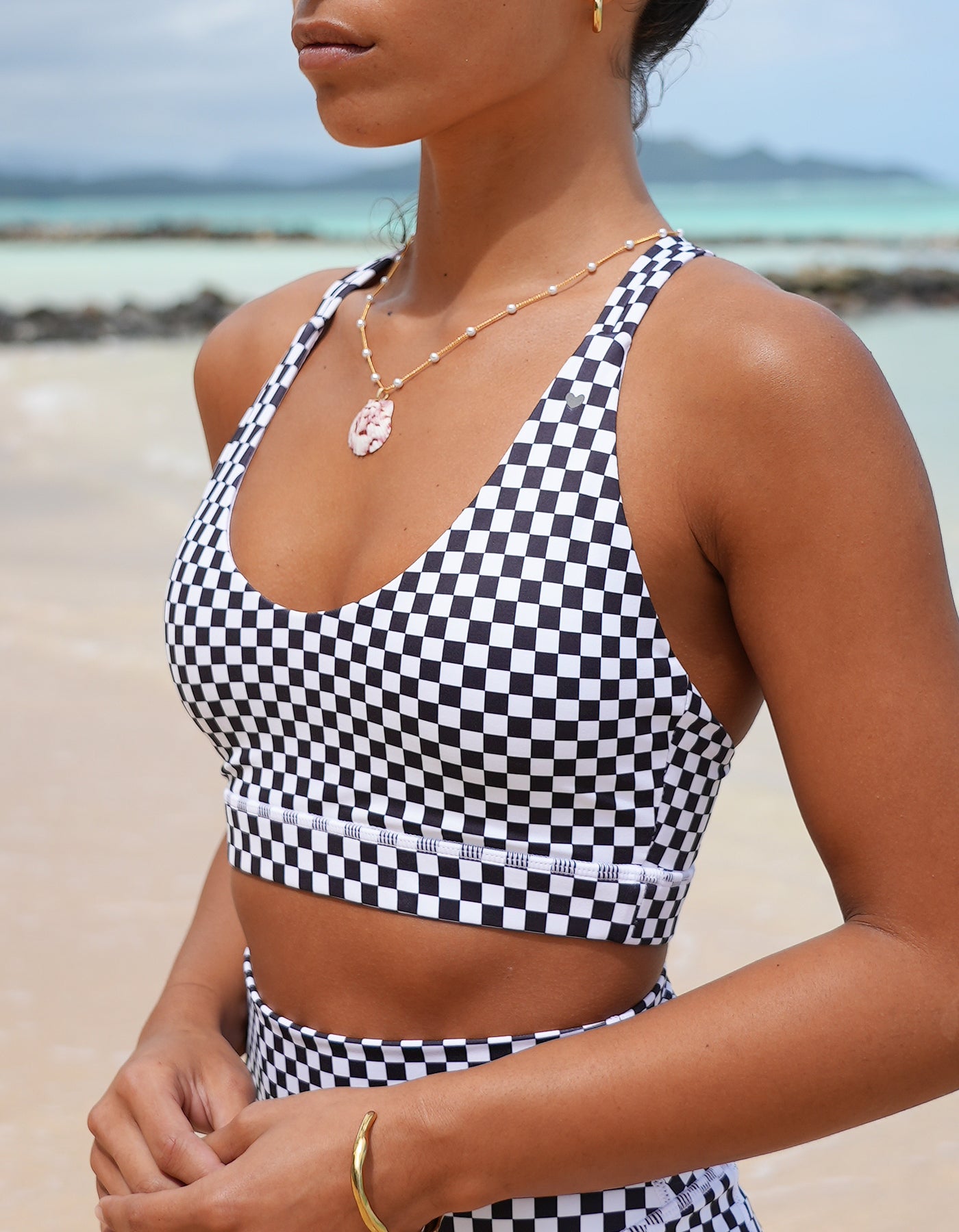 Love Fitness Johana Sports bra in a checkered black print. Person wearing a black and white checkered active wear top on a beach.