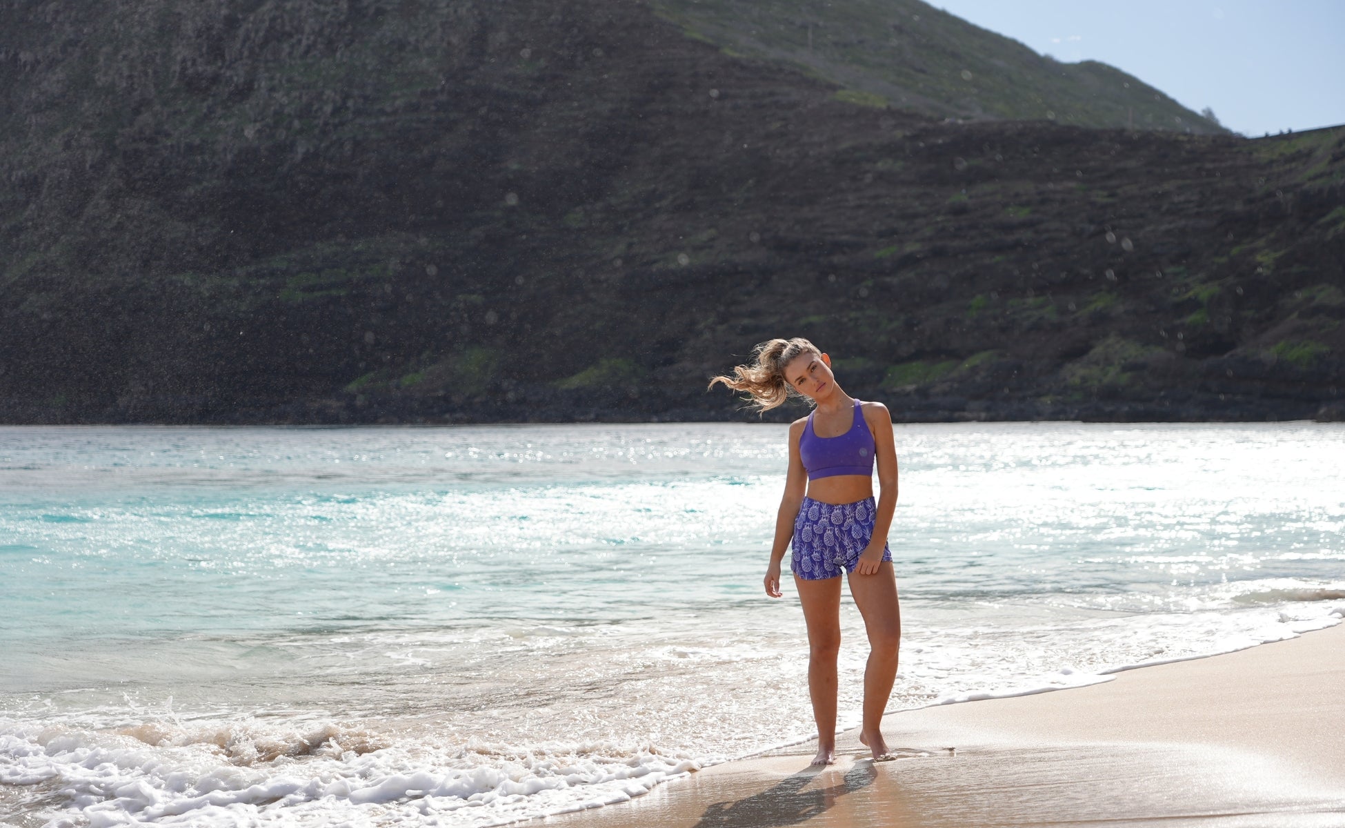 Woman in love fitness pineapple runners and leilani sports bra standing on a beach with mountains in the background