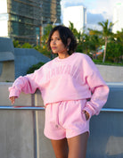 Person wearing Love Fitness State of aloha sweatshirt pink 'Hawaii' sweatshirt and shorts set, standing outdoors. Colorway is called strawberry pink matching with love fitness sweet heart sweatshorts in the same color pink.