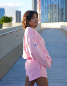 Person wearing Love Fitness State of aloha sweatshirt pink 'Hawaii' sweatshirt and shorts set, standing outdoors. Colorway is called strawberry pink matching with love fitness sweet heart sweatshorts in the same color pink.