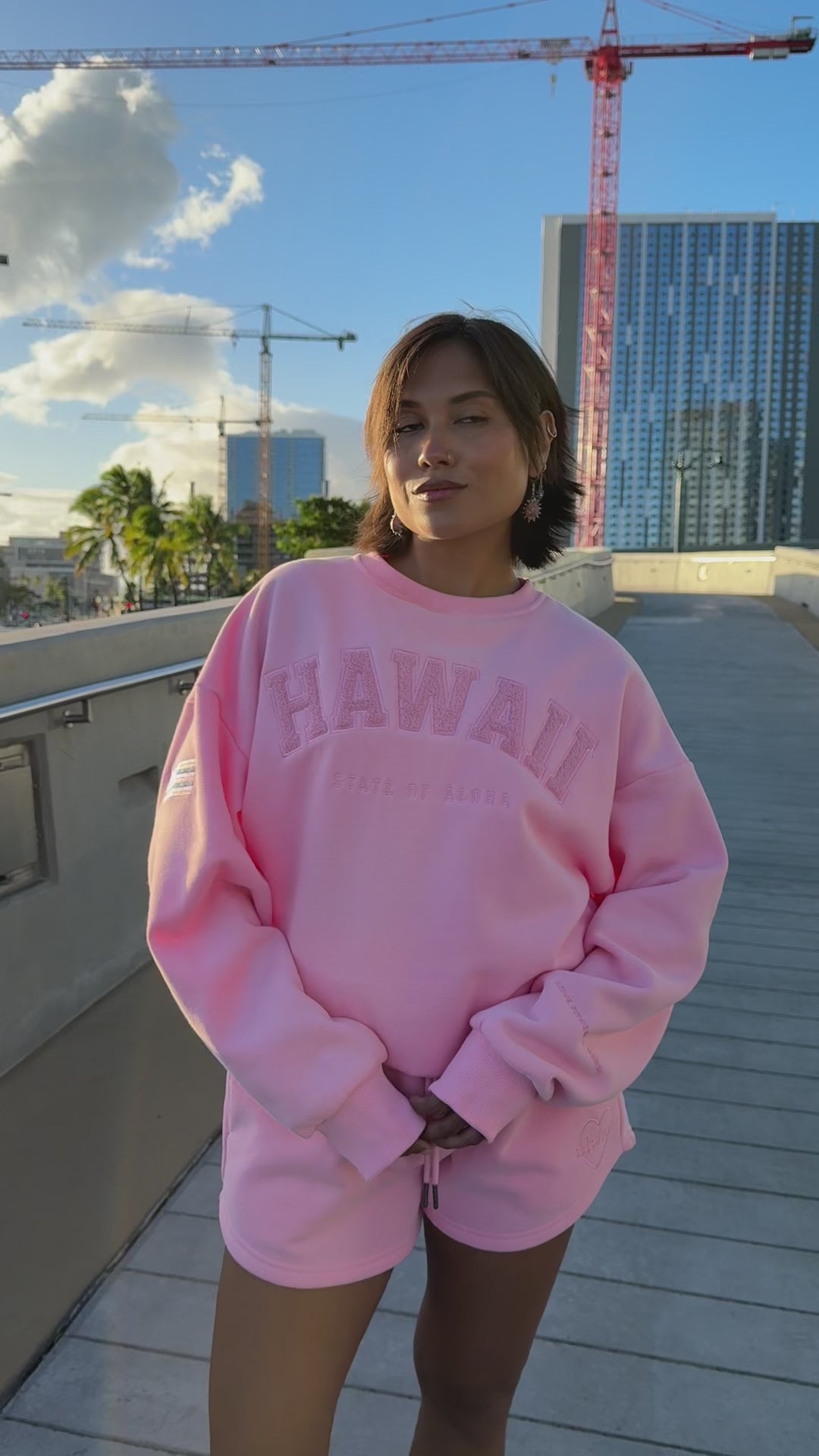 Person wearing Love Fitness State of aloha sweatshirt pink 'Hawaii' sweatshirt and shorts set, standing outdoors. Colorway is called strawberry pink matching with love fitness sweet heart sweatshorts in the same color pink.