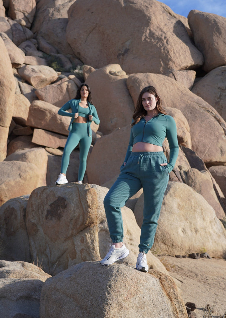 Photograph features 2 models standing on big rocks wearing Love Fitness Sedona Collection outfits of pieces in the Mineral color-way.
