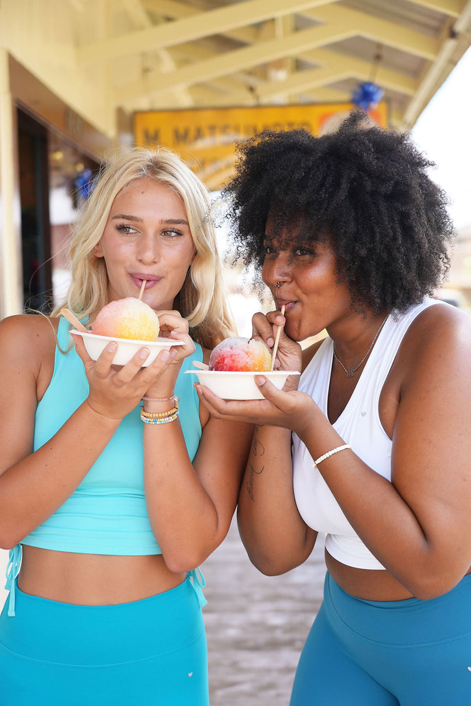 2 woman enjoying shave ice and featuring our new Melted Popsicle Collection pieces. The ethereal cinched top in 2 new colors coconut and shave ice and the new Essential leggings in the colors Sweet tart and tropsicle