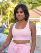 Love Fitness Eloise Sports bra in Strawberry Cream Pink. Model is standing on paved path holding side rail wearing a pink sports bra and pink sweatshorts with pockets and drawstring.