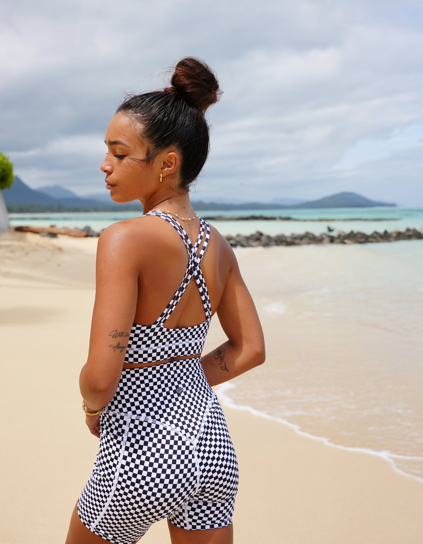 Love Fitness Johana Sports bra in a checkered black print.  Woman in a black and white checkered activewear set standing on a beach with ocean and sky in the background
