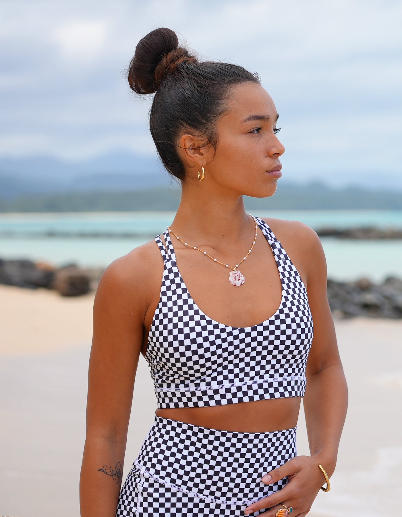 Love Fitness Johana Sports bra in a checkered black print. Woman in a black and white checkered outfit standing on a beach with ocean in the background