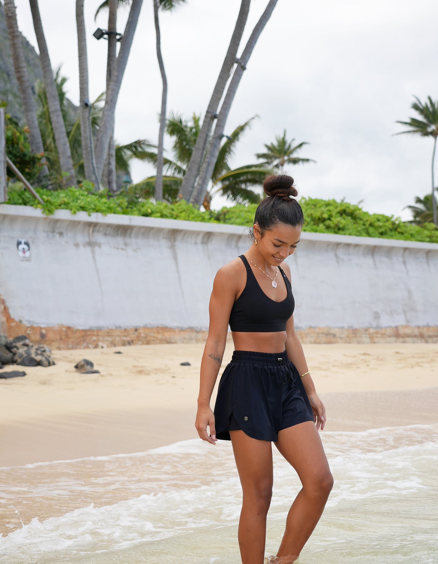Love Fitness Navi Runners and Johana sports bra in the color black (opihi)  Woman in black athletic wear standing on a beach with palm trees in the background