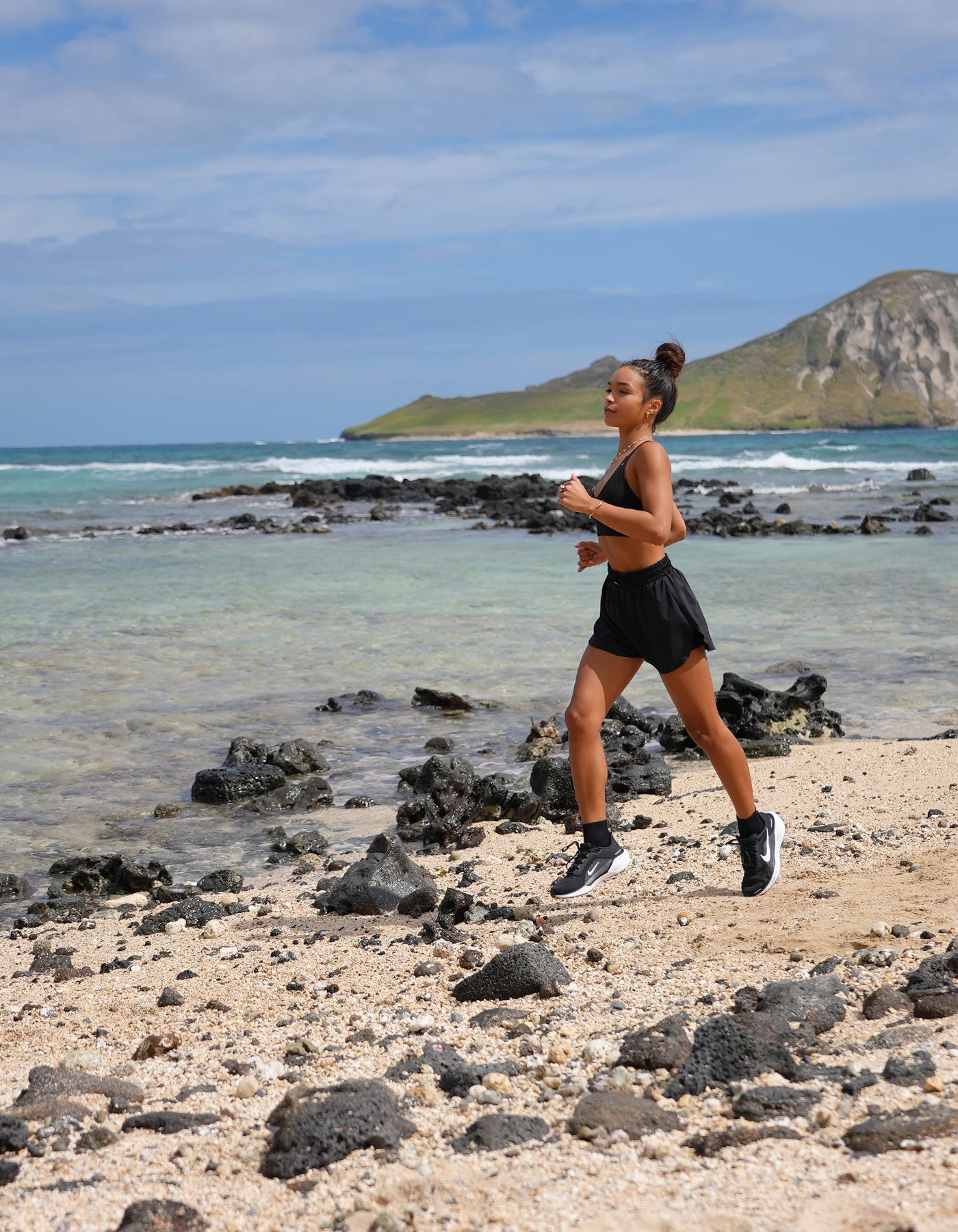 Love Fitness Navi Runners and Johana sports bra in the color black (opihi)  Person running on a beach with ocean and mountain in the background
