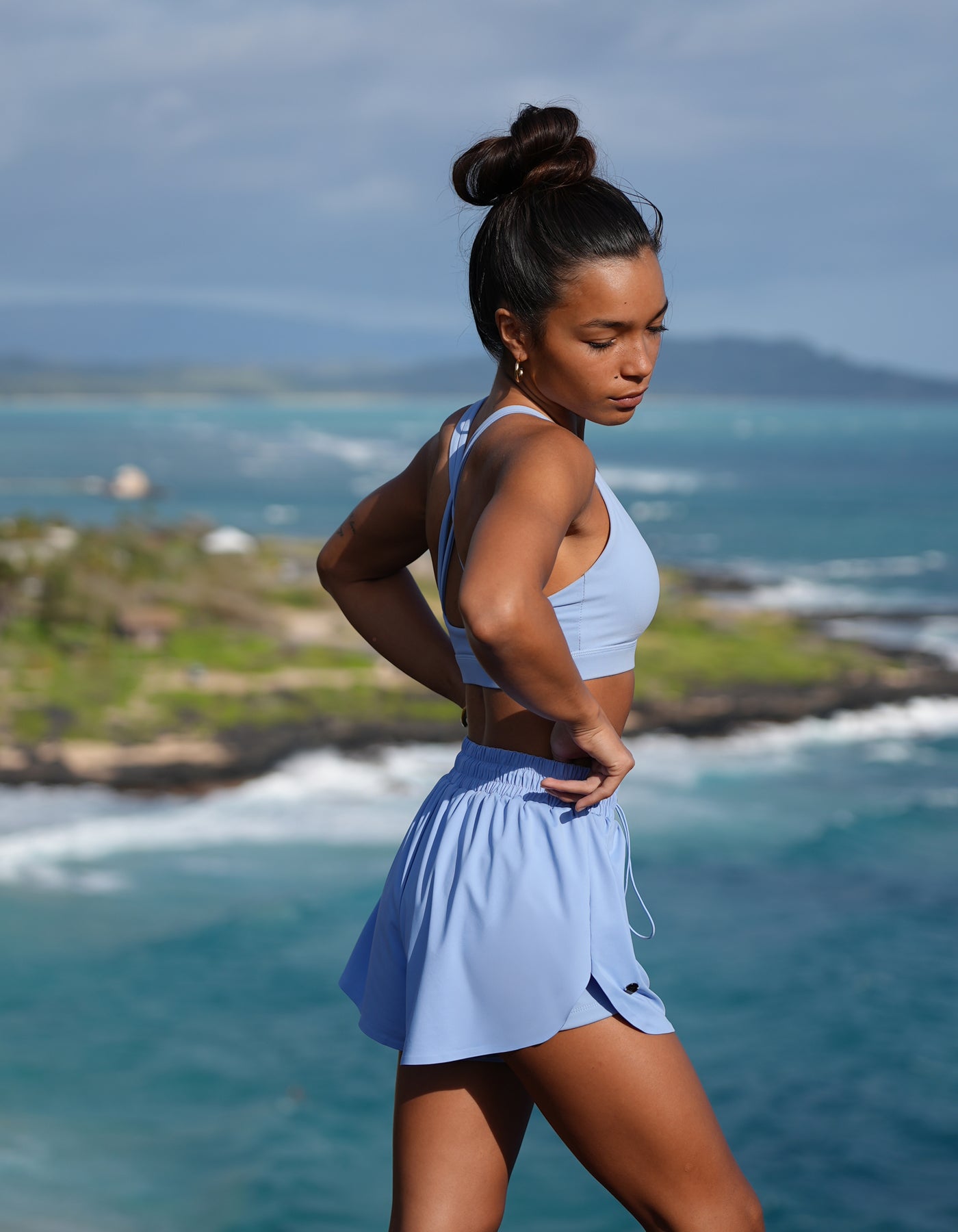 Love FItness Navi Runner in the color tidal mist. Woman in athletic wear standing by the ocean with mountains in the background