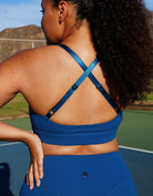 Person wearing Love Fitness Eloise Sports bra in the colorway blue opal and leggings on a tennis court