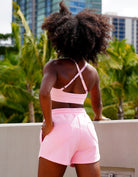Woman in pink athletic Love fitness eloise sports bra and sweet heart sweatshorts in the colorway strawberry cream posing outdoors against a stone wall.