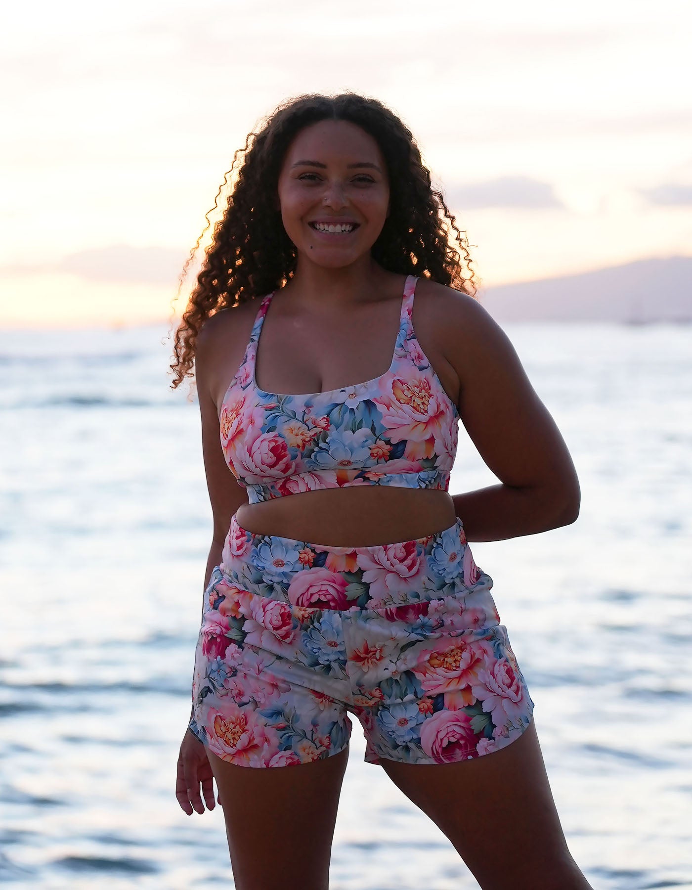 Woman wearing wearing  Love Fitness Floral Fable Runners and skye sports bra floral fable standing by the water at sunset.