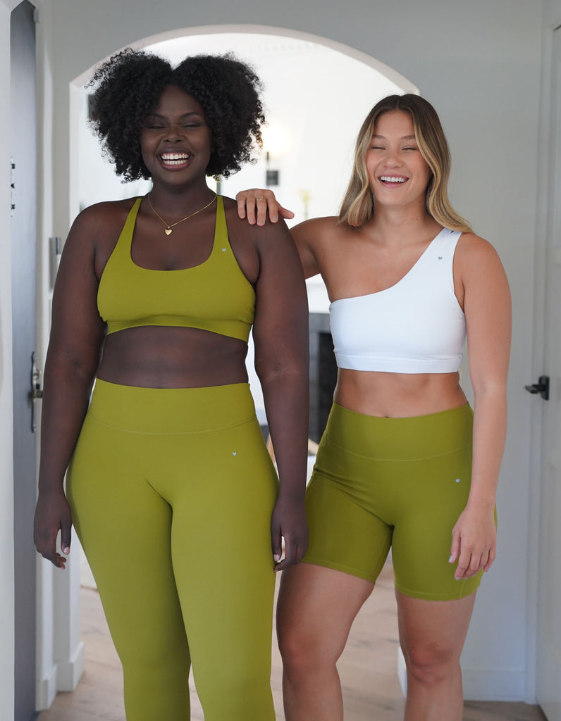 2 beautiful models of different body types and ethnicity standing next to each other smiling big and wearing activewear styles in the colors guava and lilies.