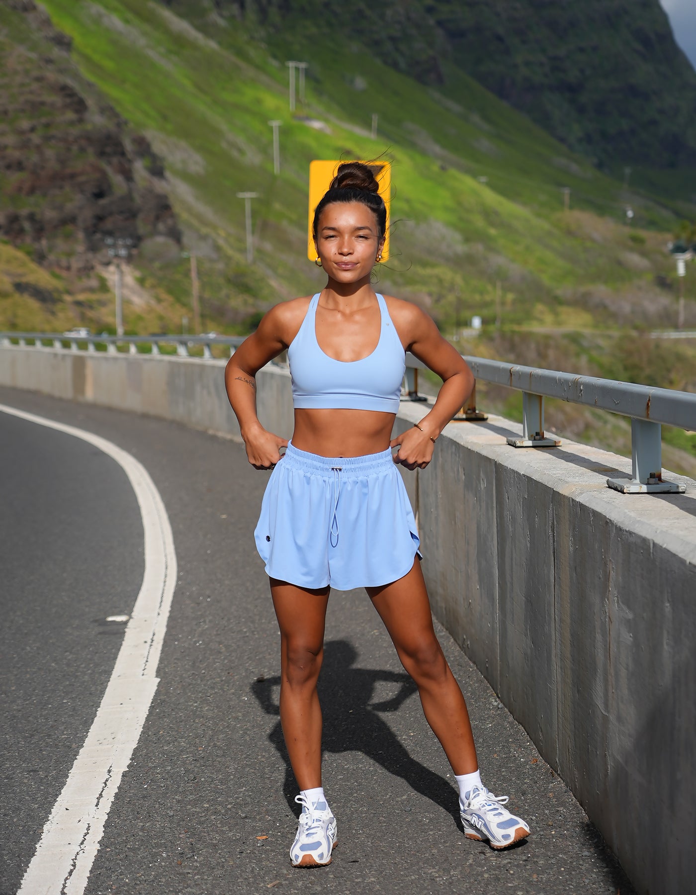 Love FItness Navi Runner in the color tidal mist.  Woman in athletic wear standing on a road with a mountainous background