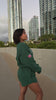 Love FItness sweet heart sweatshorts with a heart logo worn by a person, blurred background. Heart shape pockets on back and drawstring waistband. Shorts are in the color evergreen. Also wearing the state of aloha sweatshirt that has a hawaiian flag on the sleeve and embroidered words Hawaii large outline on the front with smaller text below saying state of aloha.