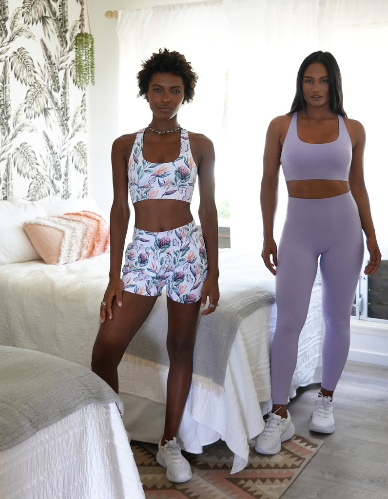 Love FitnessApparel Leilani Sports Bra in the color Blossom. Strappy detailing that is beautiful and elegant. Featuring two models of different body shapes and skin tones. One model is wearing the Island Dreams print to show the beautiful combination with the Blossom solid set