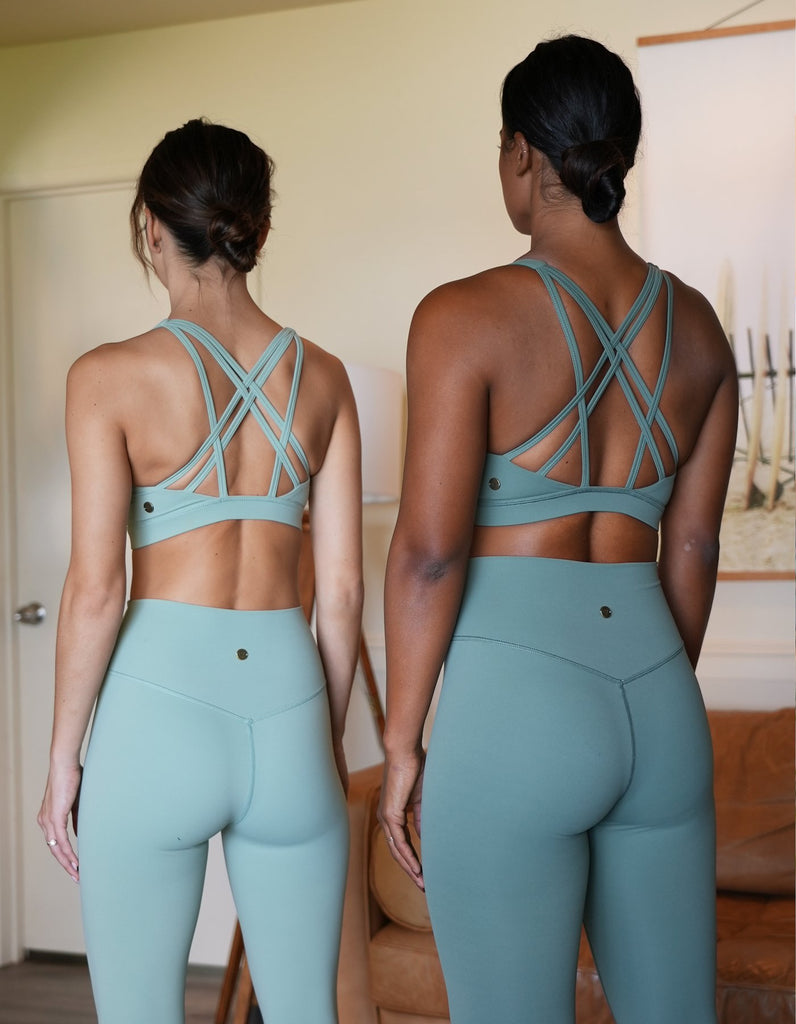 2 models standing side by side wearing the Love Fitness Leilani Sports bra with their back facing us to show the strap detailing. The leggings are smooth with a vshape seam on the back waistband