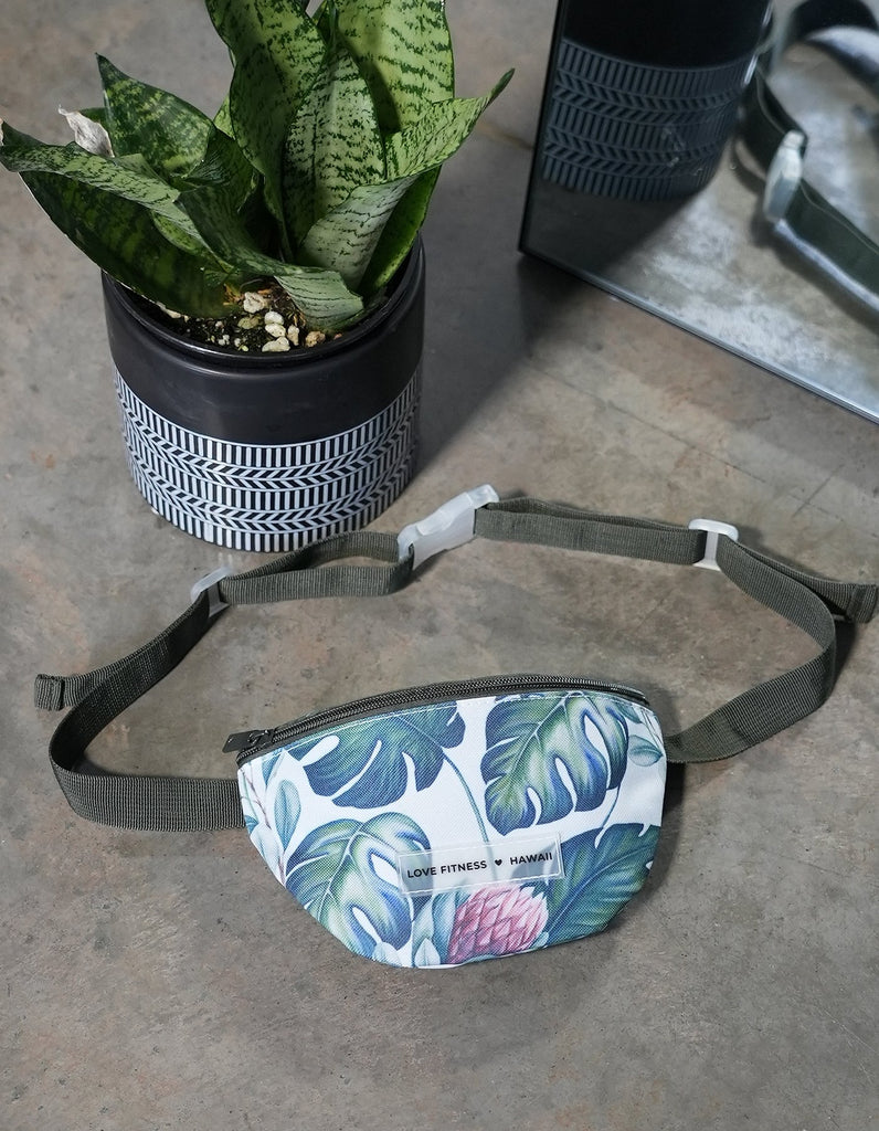 Love Fitness fanny pack in a beautiful monstera print with a silicone clear label that says love fitness hawaii.b=
